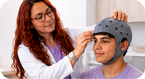 Adolescente con equipo de neuromodulación cerebral mientras una profesional ajusta el dispositivo durante la sesión.